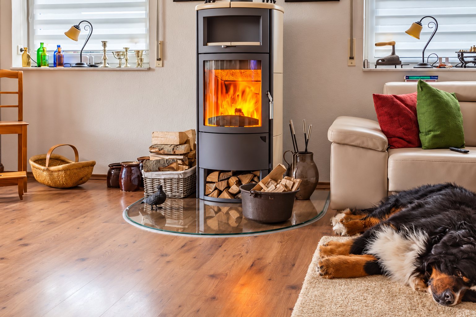 Un poêle à bois gris avec une flamme visible chauffe un salon lumineux où un bouvier bernois dort sur un tapis près d'un canapé en cuir.