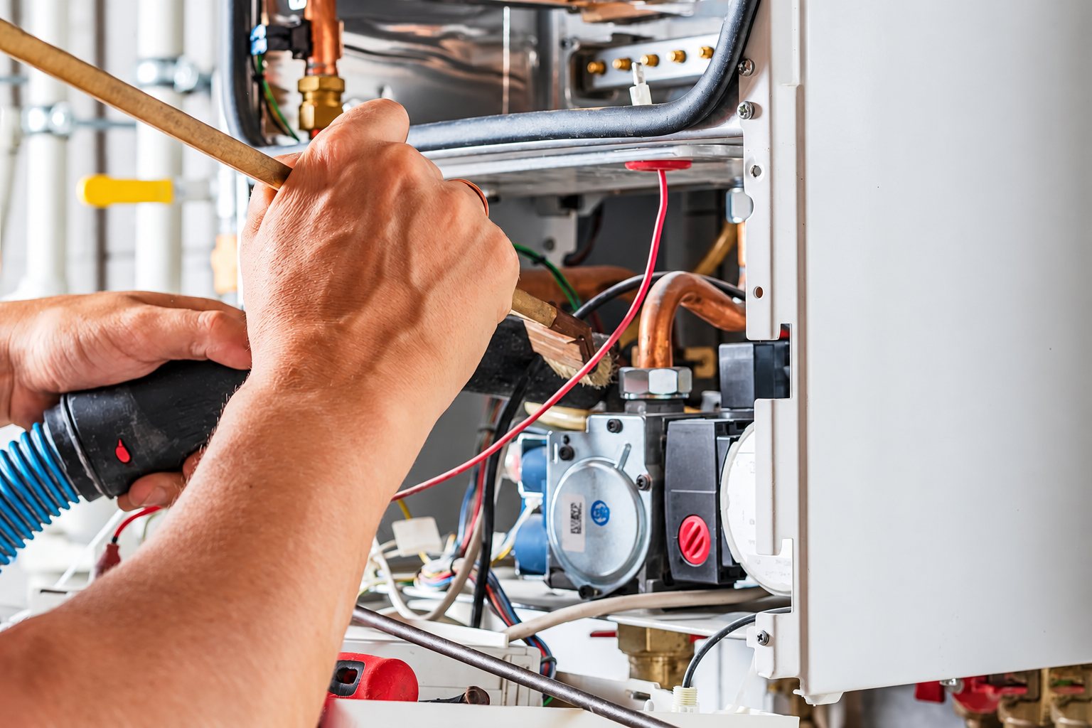 Gros plan sur les mains d'un technicien qui répare l'intérieur d'une chaudière avec un chalumeau et une baguette de brasage.