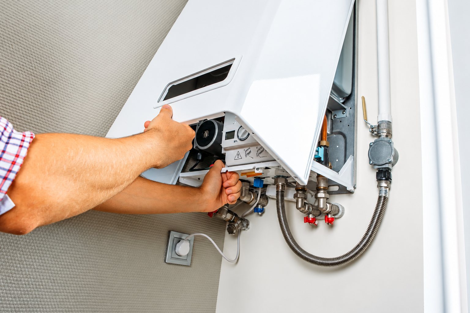 Les mains d'un technicien soulèvent le capot blanc d'une chaudière murale pour accéder aux tuyaux et aux raccords.